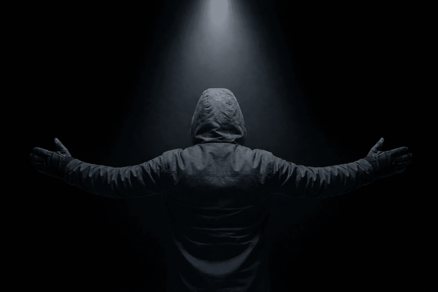 A hooded figure standing beneath a spotlight